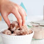 A hand pulling one rum ball out of a bowl full of them.