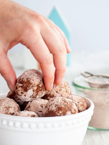 A hand pulling one rum ball out of a bowl full of them.