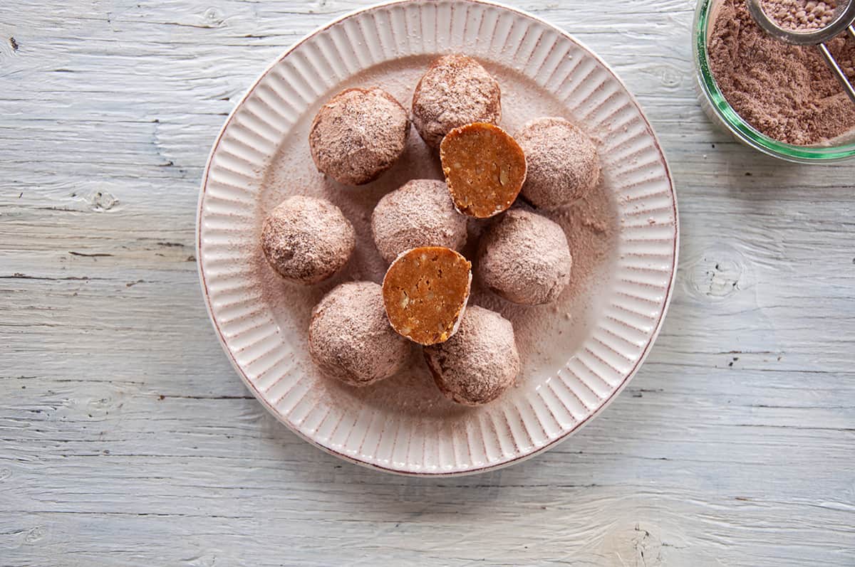 A plate filled with rum balls and one of the rum balls cut in half so that the cross section shows.