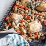 Baked Italian Chicken Thighs on a baking pan with carrots, potatoes, a wooden spoon and fresh rosemary.