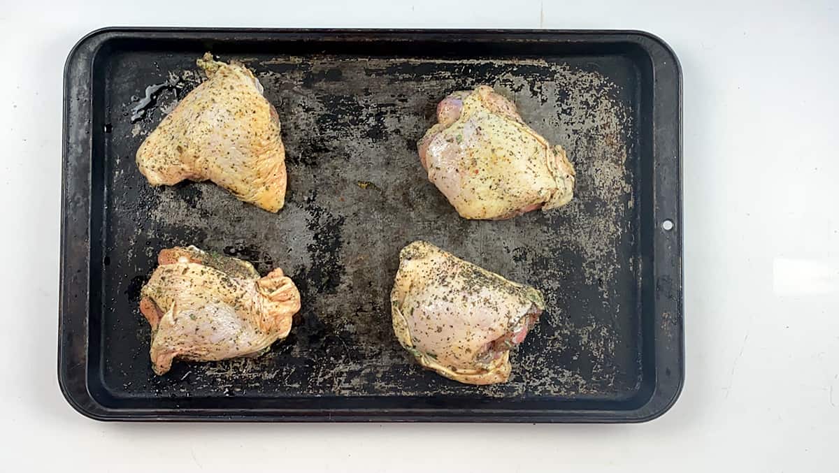 Four uncooked chicken thighs getting ready for the oven.