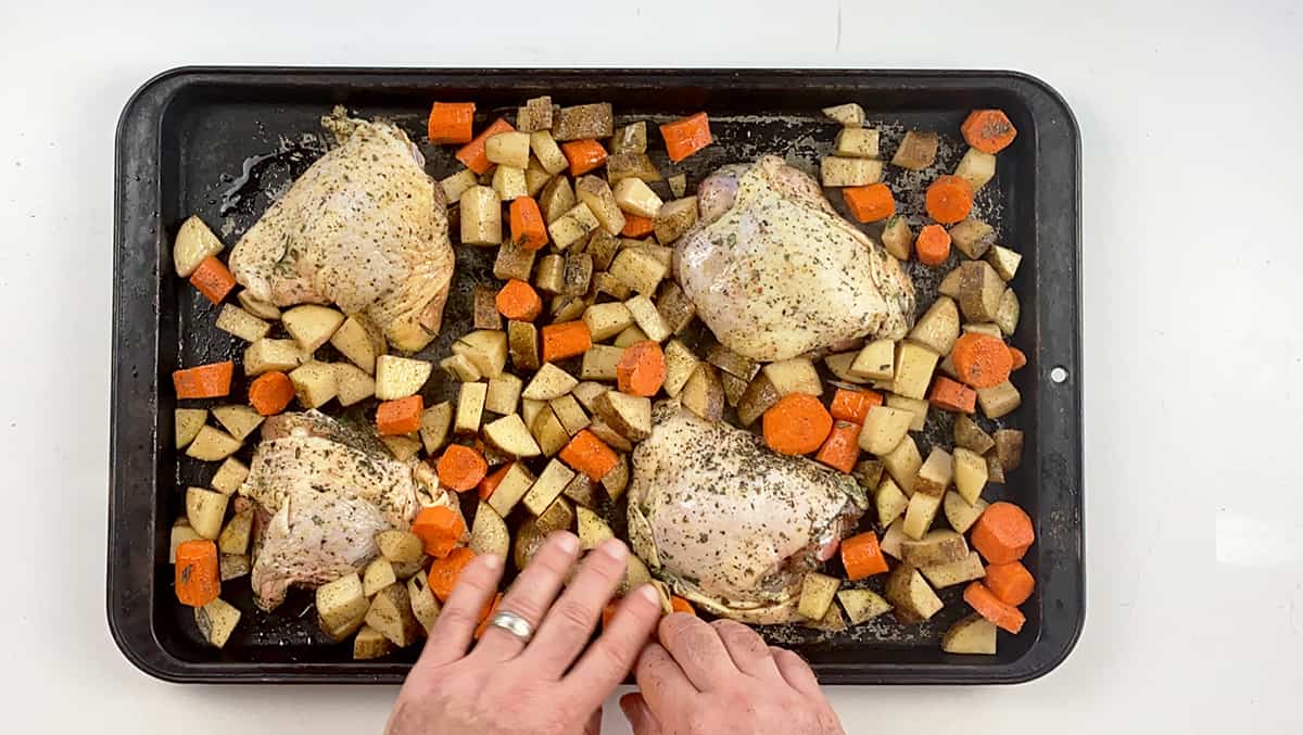 Chicken thighs, potatoes, and carrots all spread out on a baking pan.