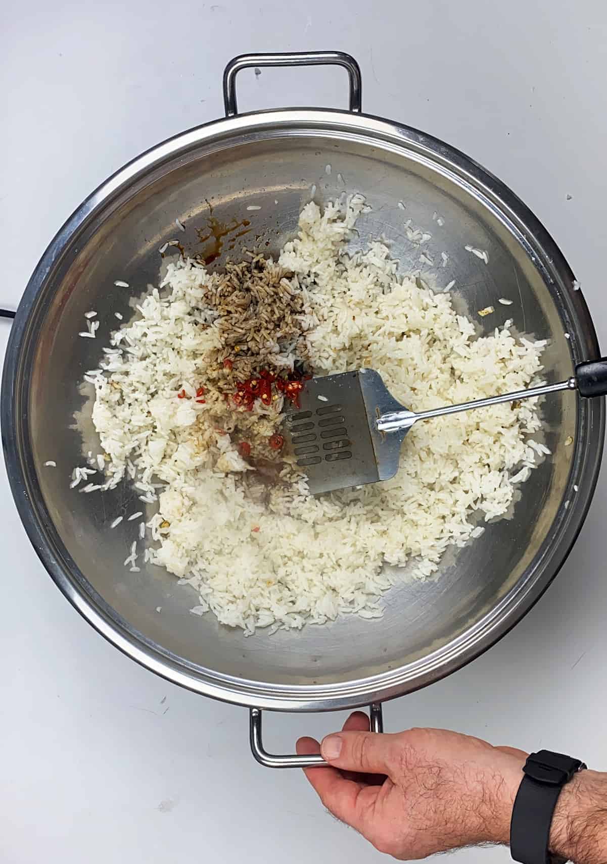 Vigorously stirring rice, pepper, and asian sauces in heated wok.