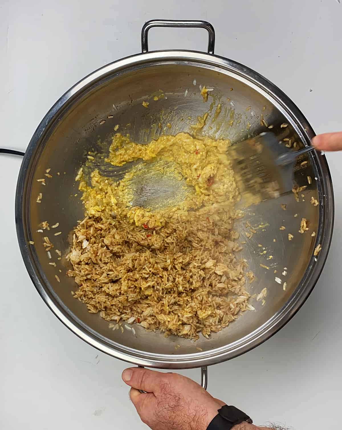 Vigorously stirring eggs in wok while rice is sitting on the side of a wok.