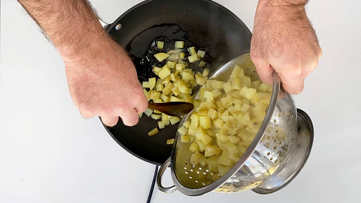 Pouring parboiled potatoes into a frying pan with bacon grease.