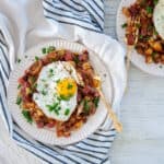 Corned Beef Hash on a white plate with a single sunny side up egg on top.