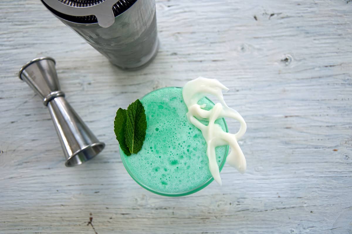 Overhead image of a grasshopper cocktail in a coupe glass with a measuring jigger off to the side.