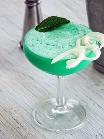 Grasshopper drink an a coupe glass with a mint leaf and white chocolate garnishing the cocktail.