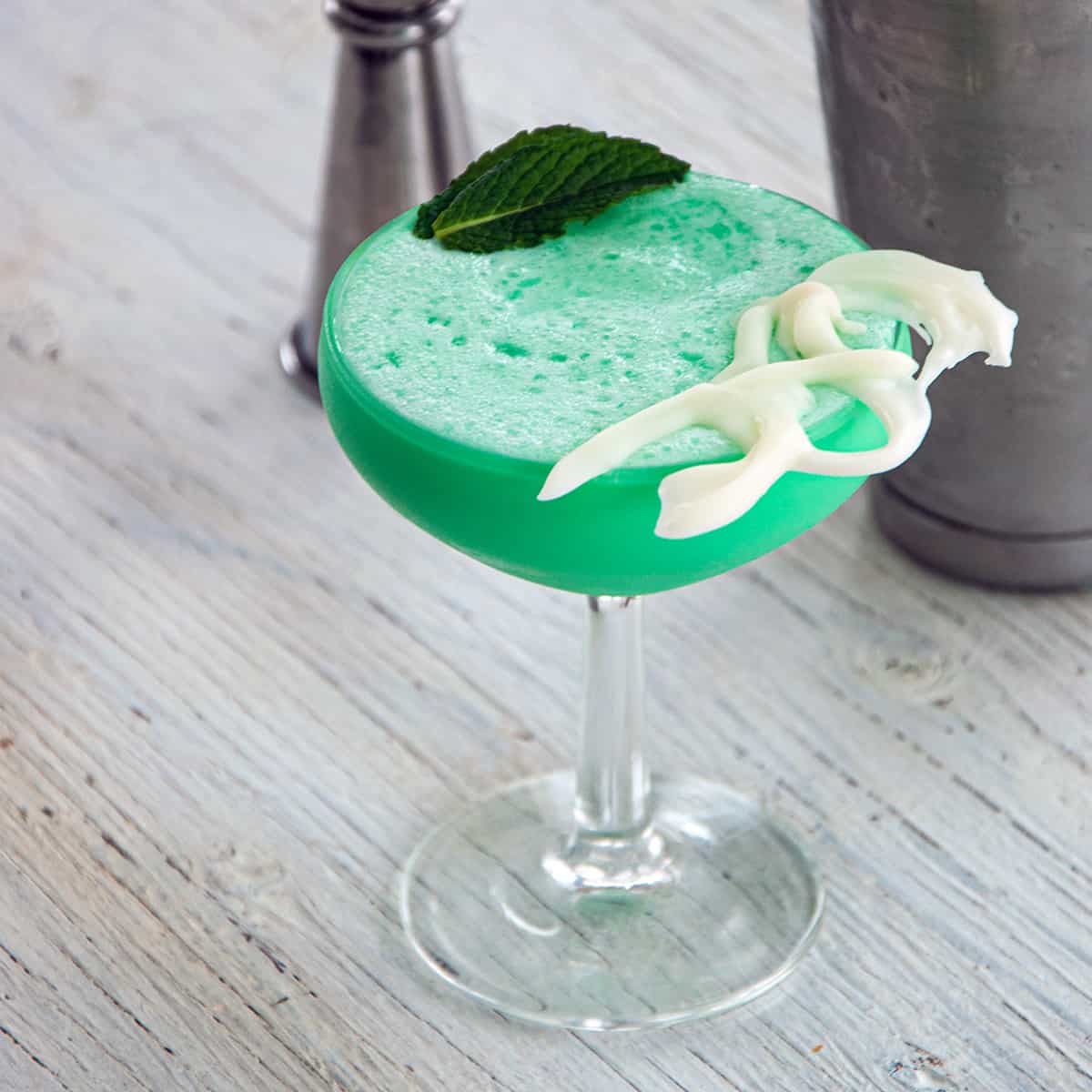 Grasshopper drink an a coupe glass with a mint leaf and white chocolate garnishing the cocktail.