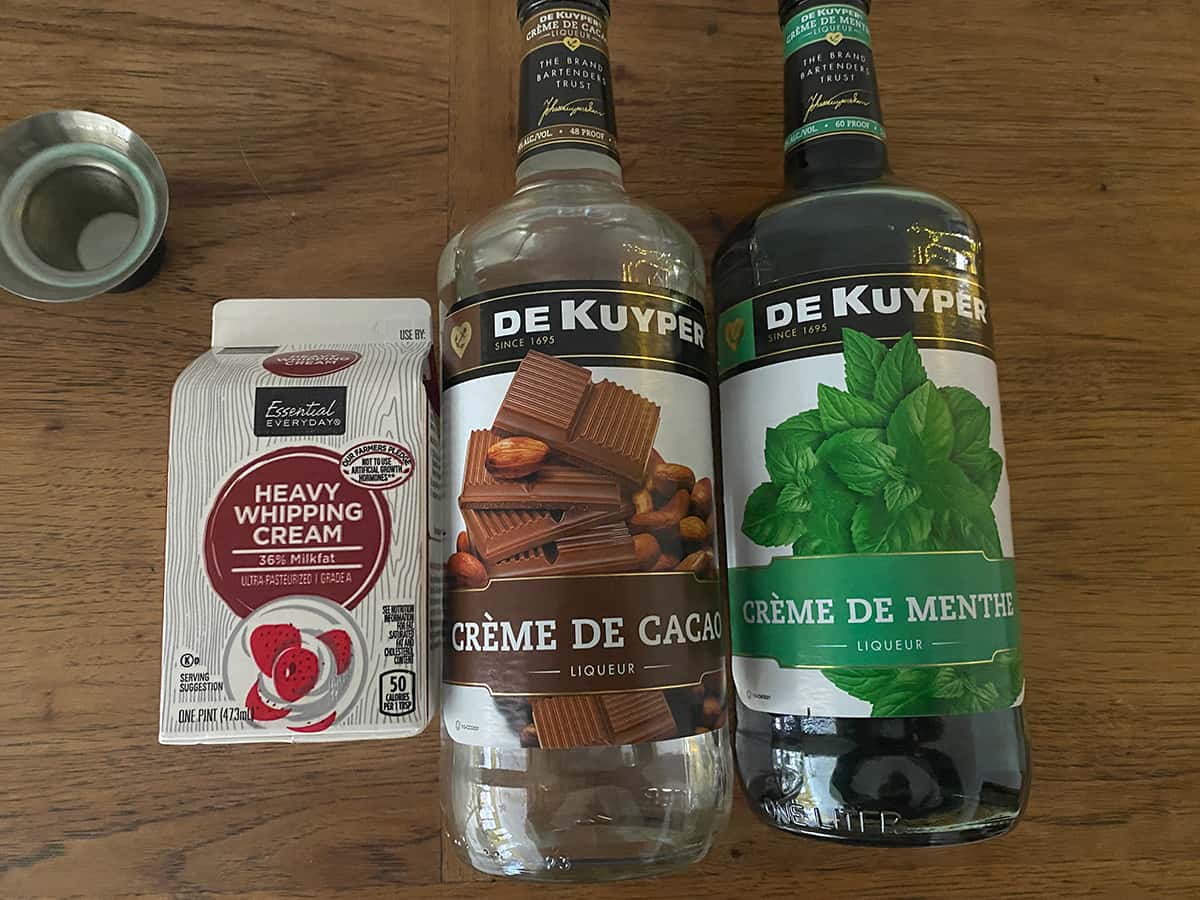 A carton of heavy whipping cream, Creme De Cacao, and Creme De Menthe on a table.