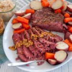 Full sous vide corned beef roast on a large serving platter with potatoes and carrots all around the sides of the roast.