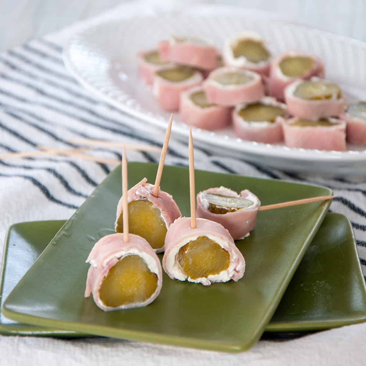 Four pickle wraps on a green plate with a platter of them in the background.