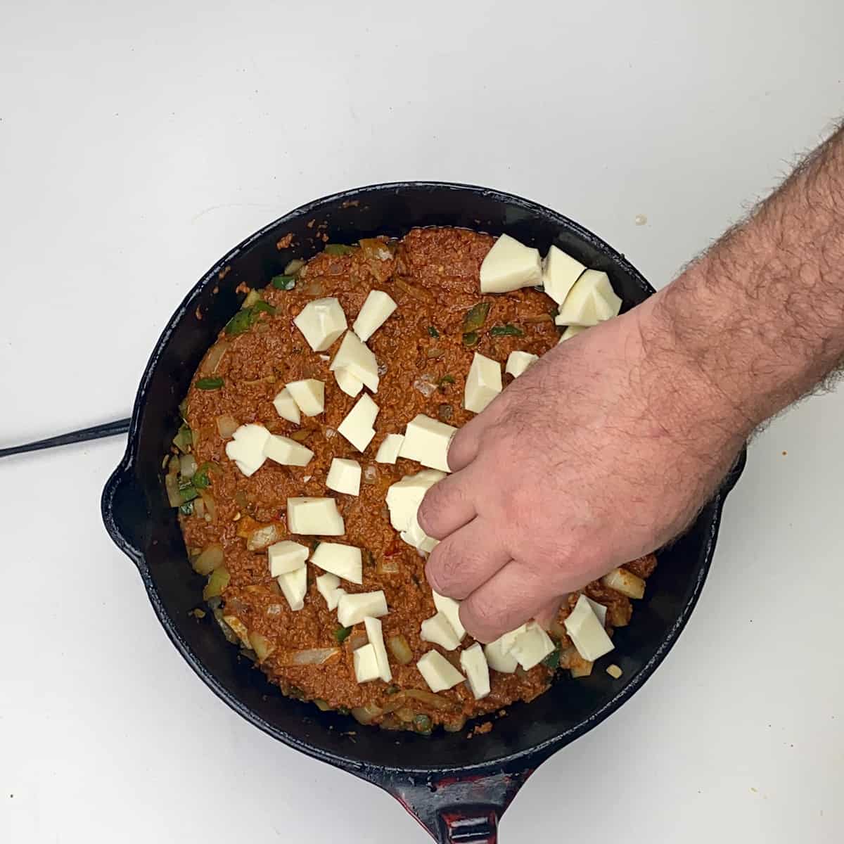 A hand over the cast iron skillet dropping in Oaxaca chese.