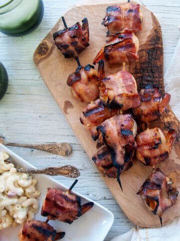 Three skewers of bacon wrapped shrimp on a wood cutting board.