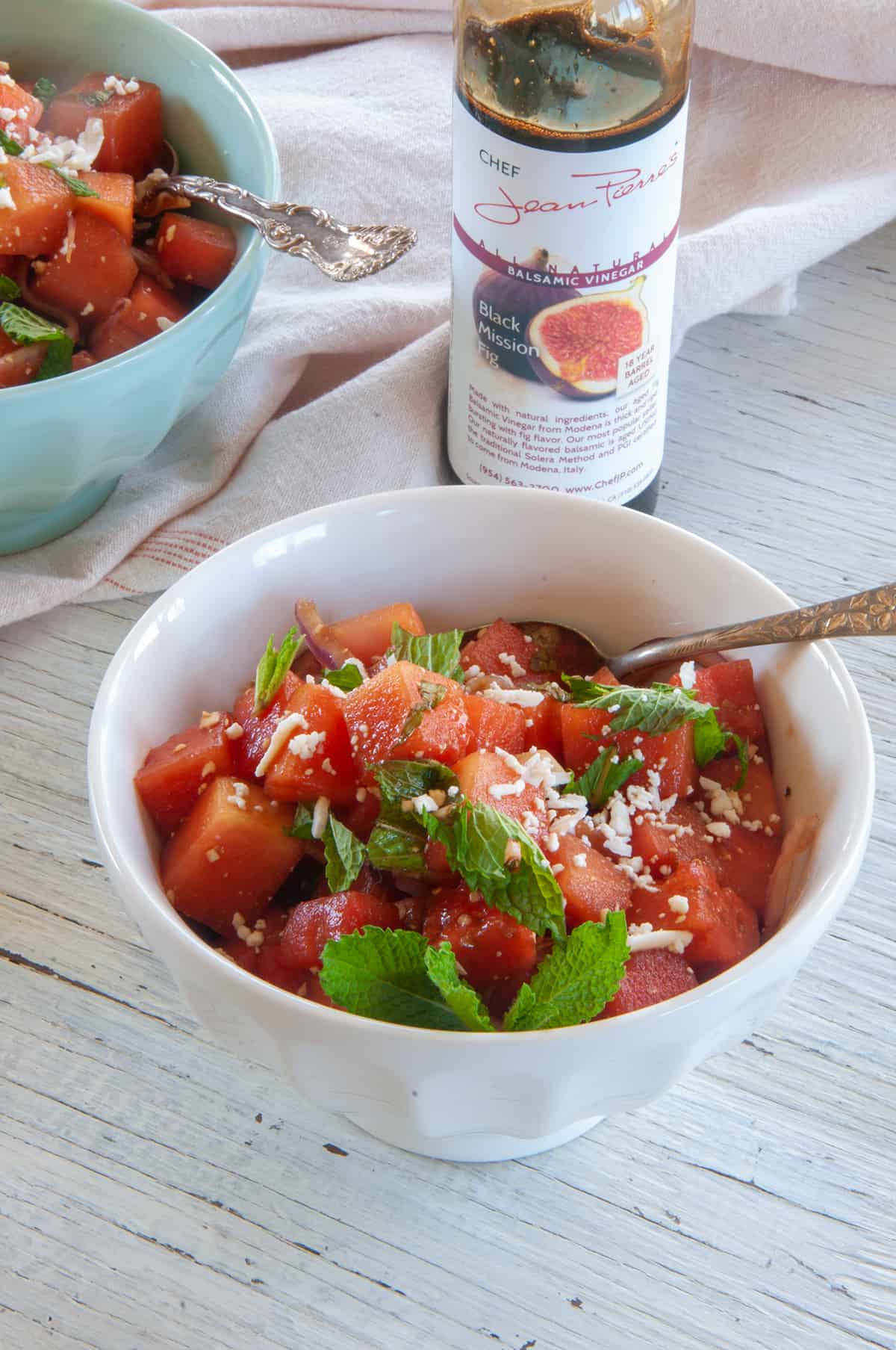 Bowl of watermelon feta salad and a jar of Black Mission Fig balsamic vinegar in the background.