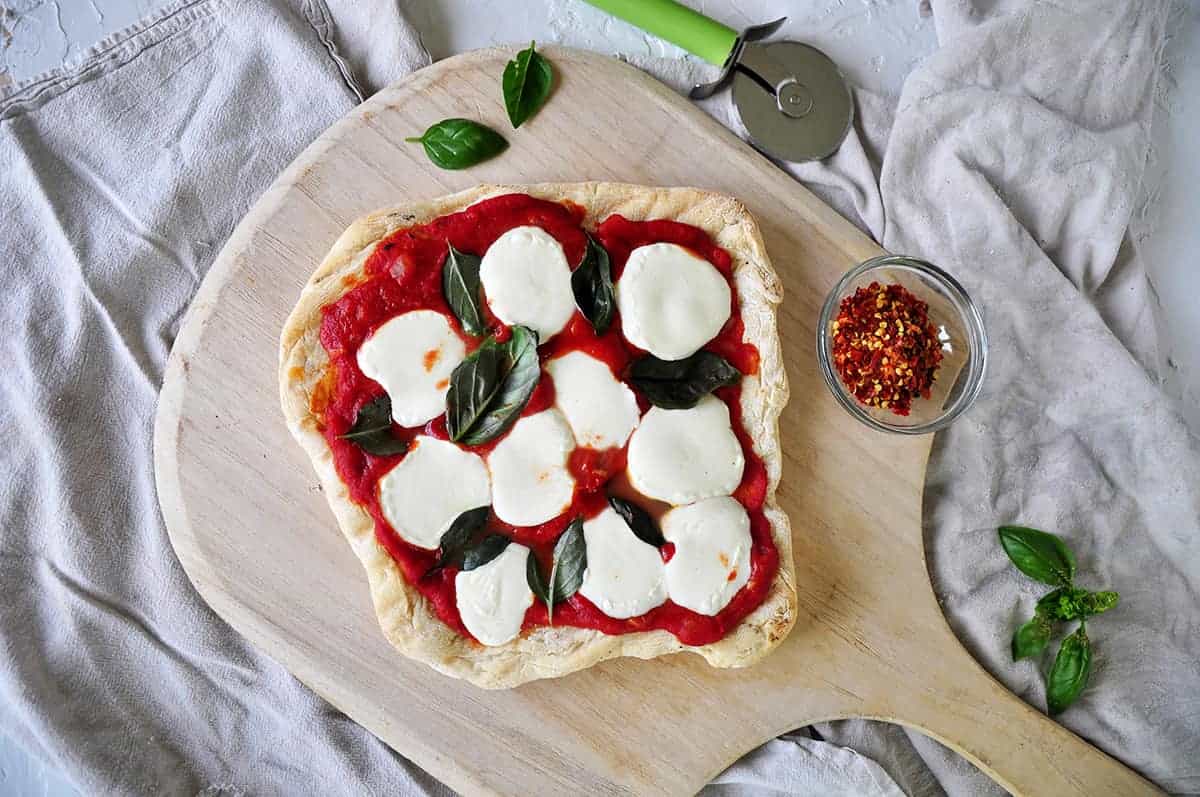 Full weber pizza on a wood pizza peel with basil and red pepper to the side. 