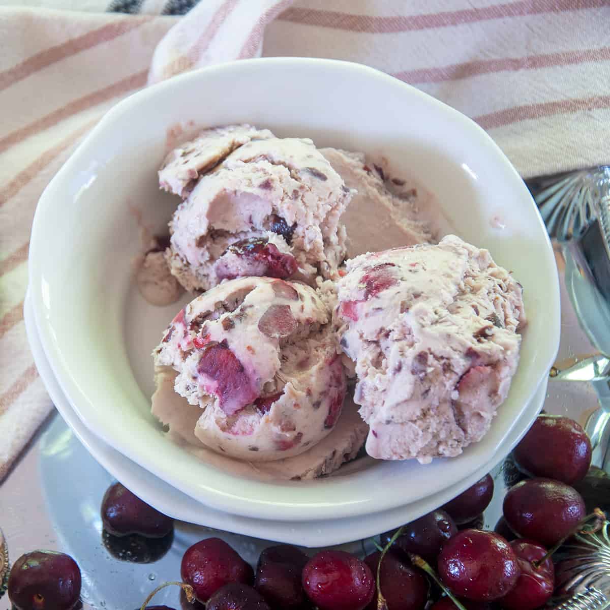 Three Scoops of No-Churn Black Cherry Ice cream in a bowl with fresh cherries to the side.