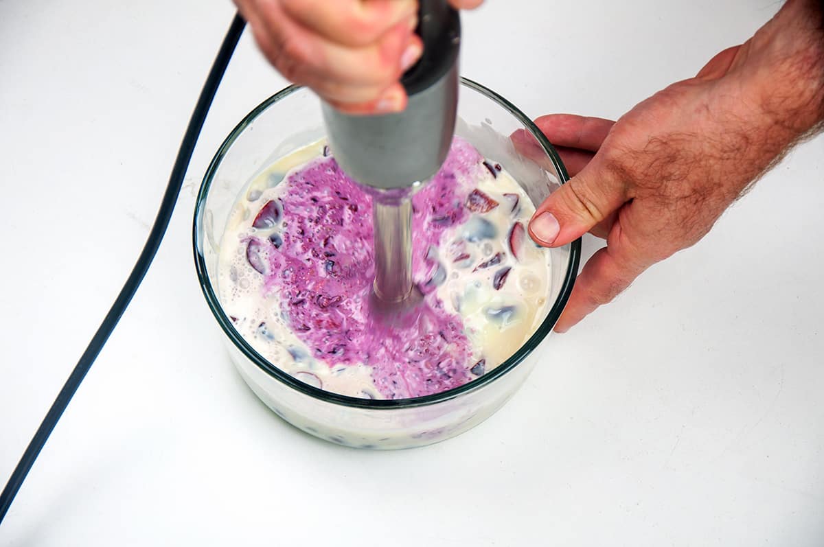 Cherries, heavy cream, and condensed milk being blended with an immersion blender.