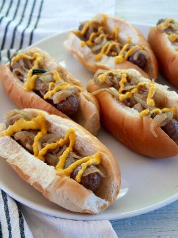 Five brats in buns and topped with onions and mustard.