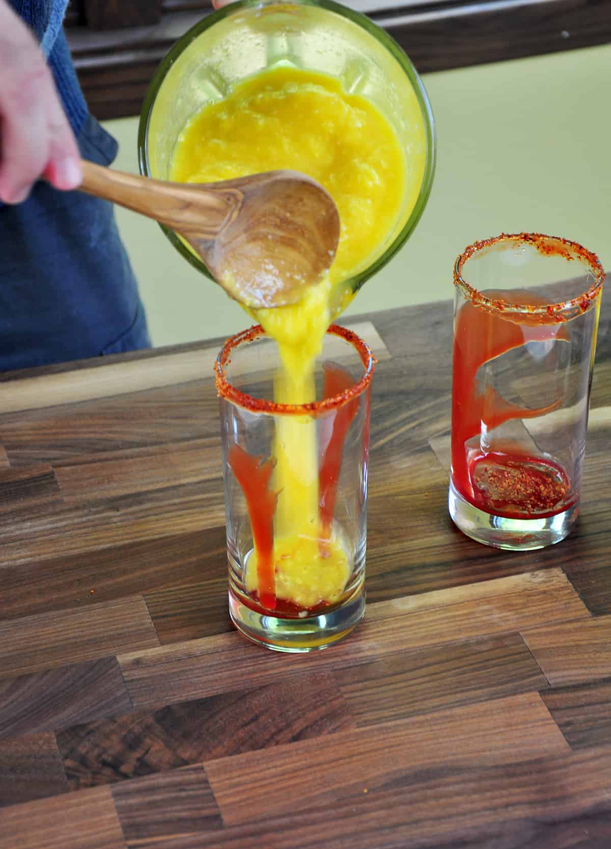 Pouring Mango mixture into a glass that has already been rimmed and has chamoy in the bottom.