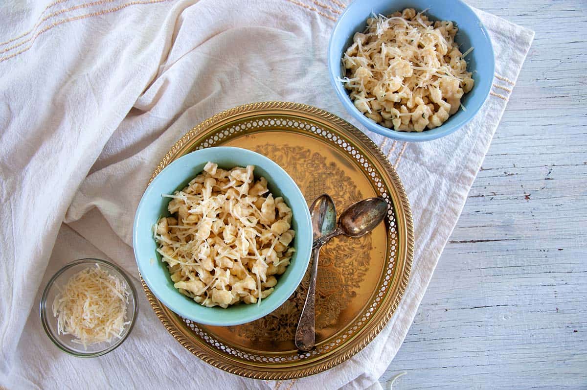 Spaetzle in a bowl on a gold platter with two spoons.