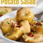 German Potato Salad in a white bowl with a fork lifting a bite out.