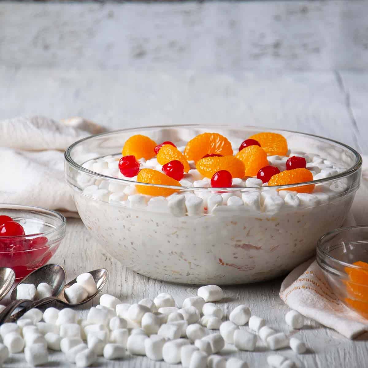 Large bowl of frog-eye salad with marshmallows, cherries, and tangerine segments on the side.