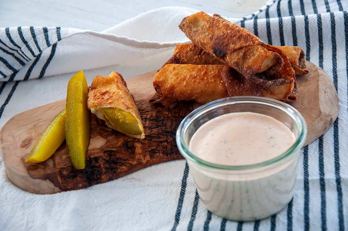 Three full cheesy fried pickles and half one on a wood cutting board.