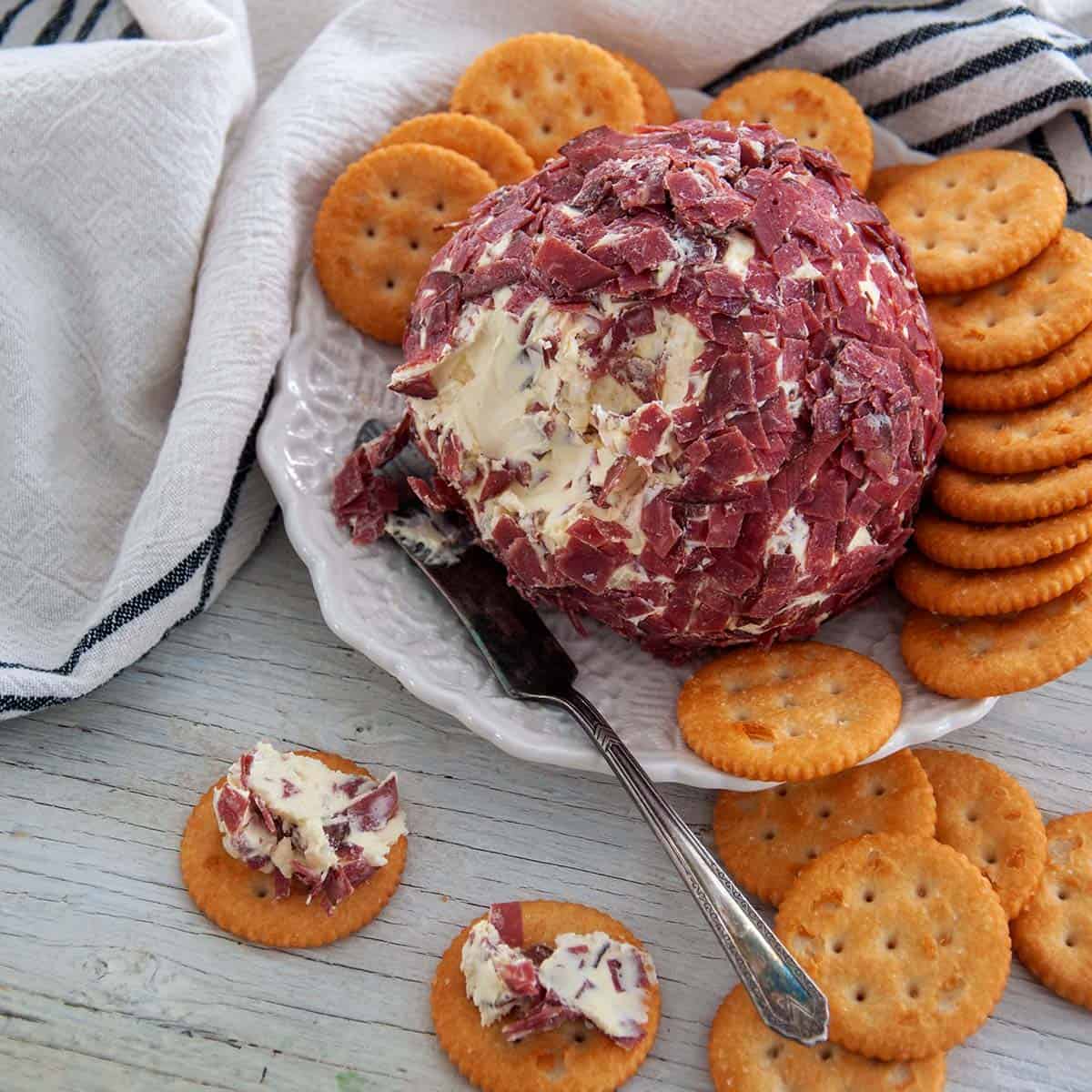 Cheeseball with dried beef on a white plate and two Ritz crackers with the dip on it.