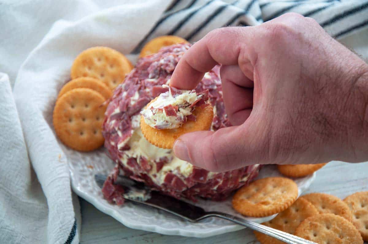 A hand holding up a Ritz Cracker with some of this Cheeseball on it.