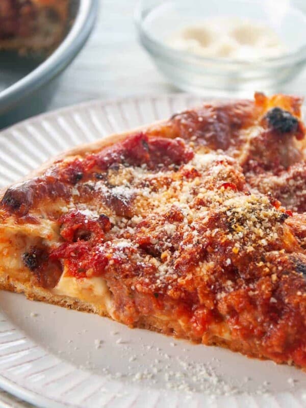 Chicago Deep Dish Pizza on a white table and a dish of cheese to the side.