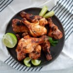 Several grilled chicken legs on a dark plate with mint and lime to the side.