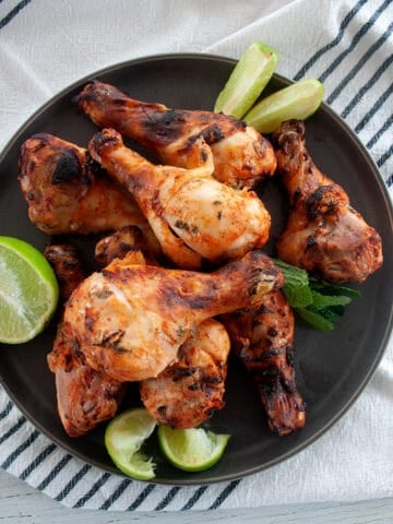Several grilled chicken legs on a dark plate with mint and lime to the side.