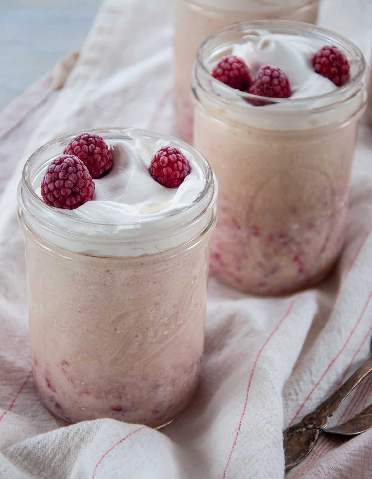 Three mason jars full of raspberry bavarian cream that is topped with whipped cream and fresh raspberries.