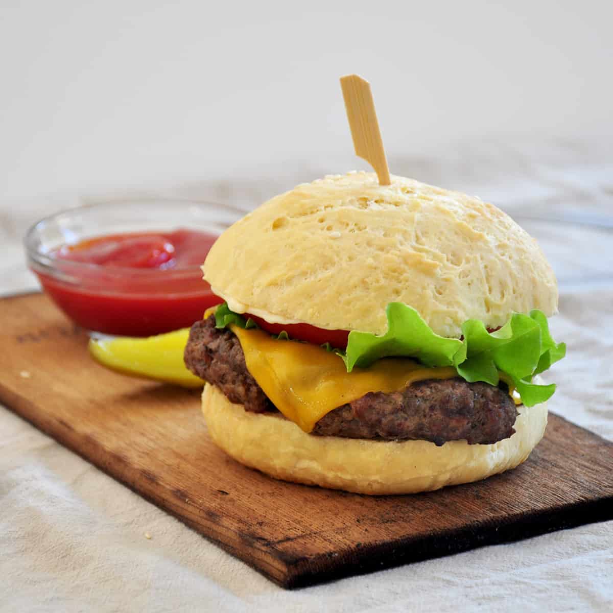 Food processor ground patty burgers on a wood plank with a pickle and ketchup in the background.