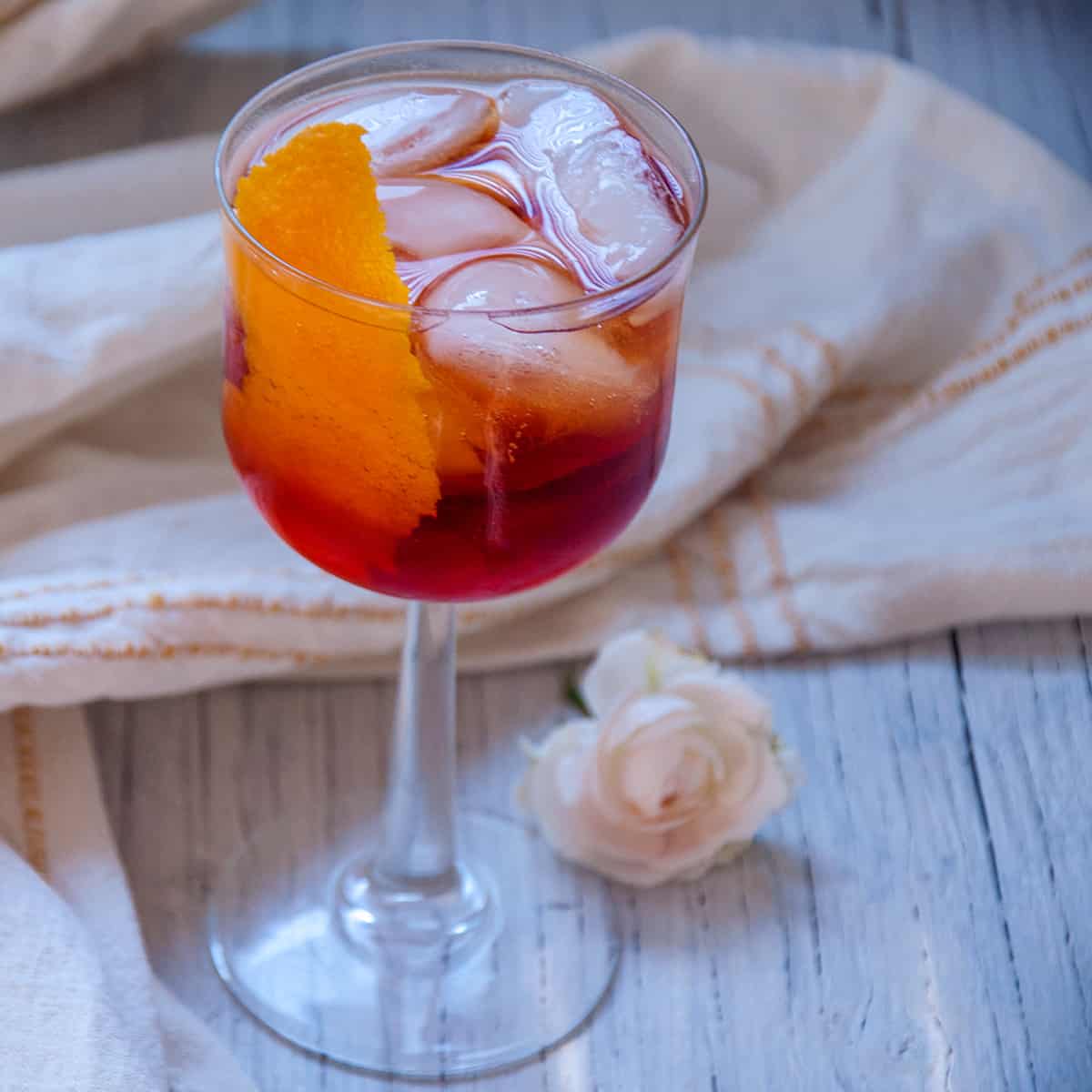 Aperol Americano in a glass on a white table with a flower.