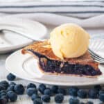 Slice of blueberry pie on a white plate with a scoop of vanilla ice cream.