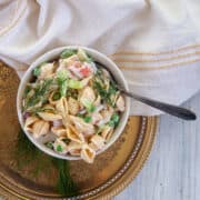 Crab pasta salad in a white bowl on a gold platter.
