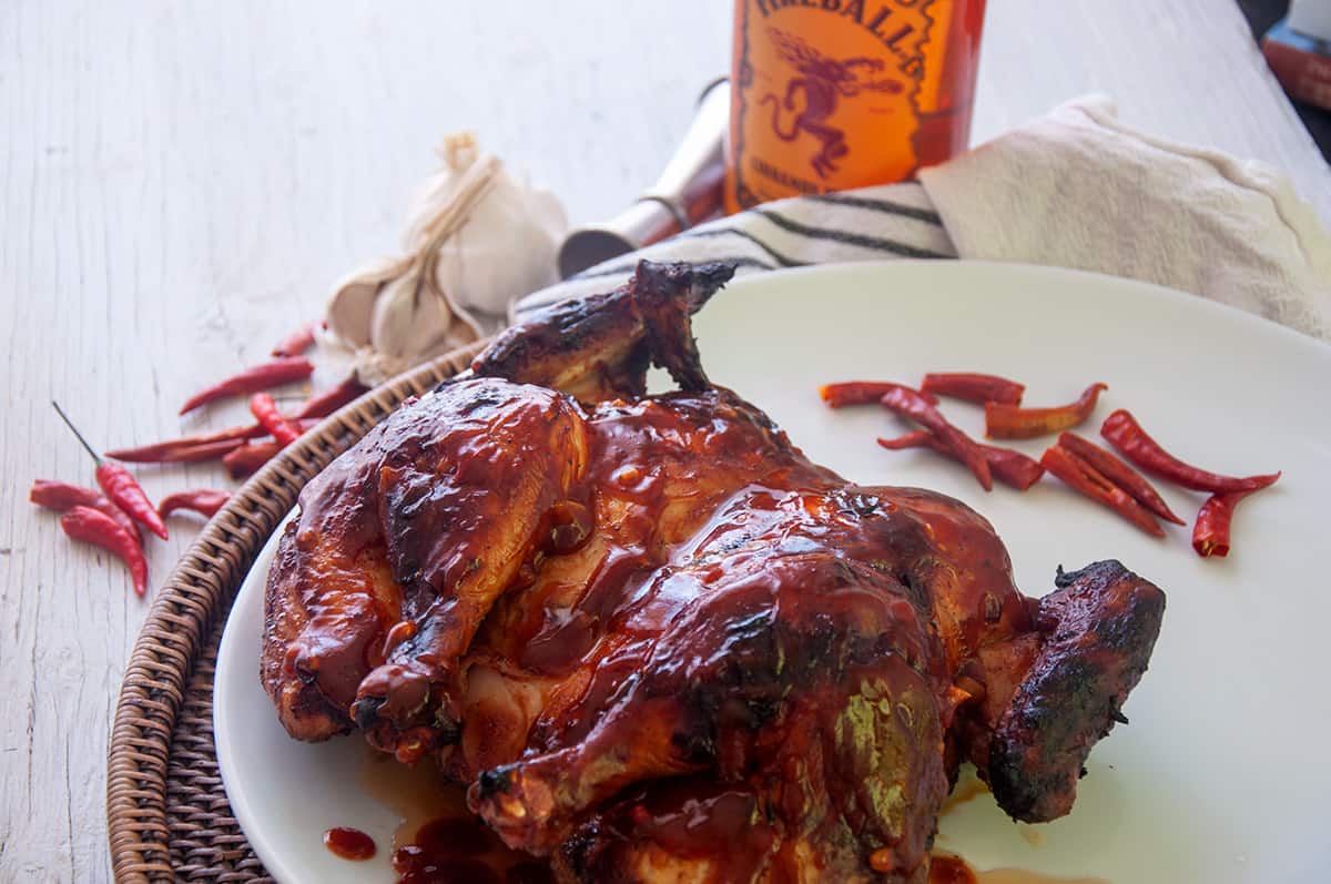 A whole spatchcocked grilled chicken that is covered with bbq sauce.