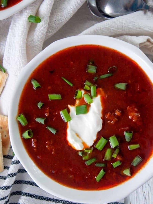 Chili con Carne in a white bowl topped with sour cream and green onions.