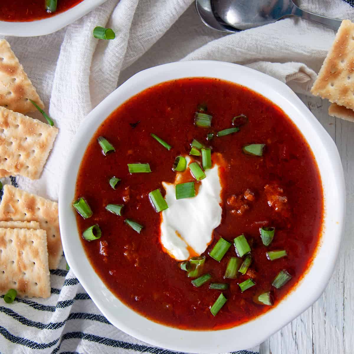 Chili con Carne in a white bowl topped with sour cream and green onions.