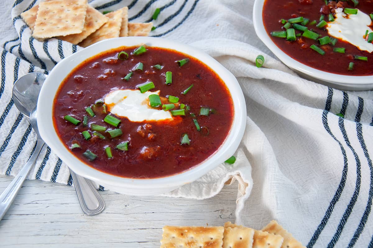 Bowl of chili on a white table with crackers and sour cream.