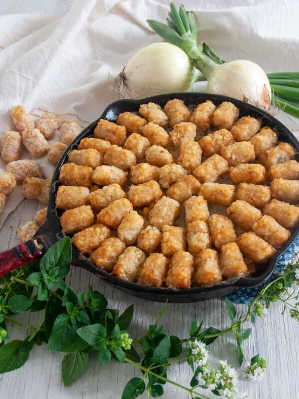 Cast iron tater tot hotdish on a wood table with some oregano.