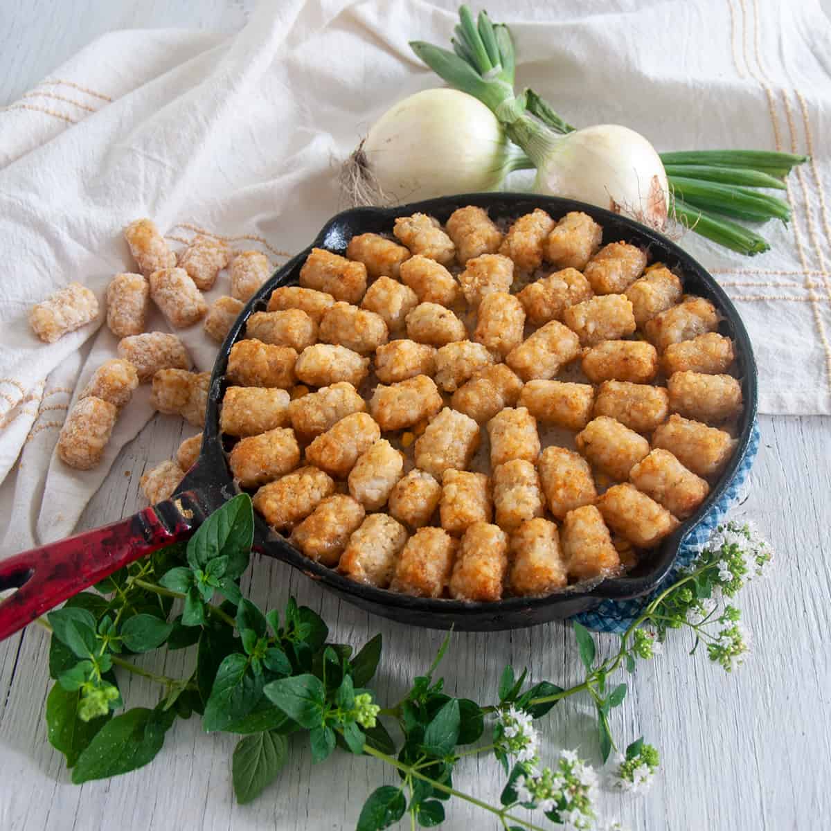 Cast iron tater tot hotdish on a wood table with some oregano.