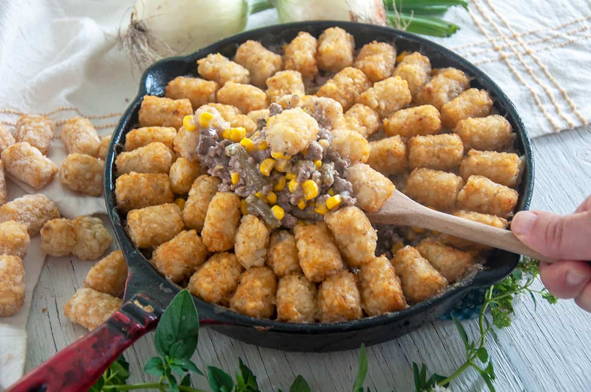 Spooning up tater tot hotdish from a cast iron skillet.