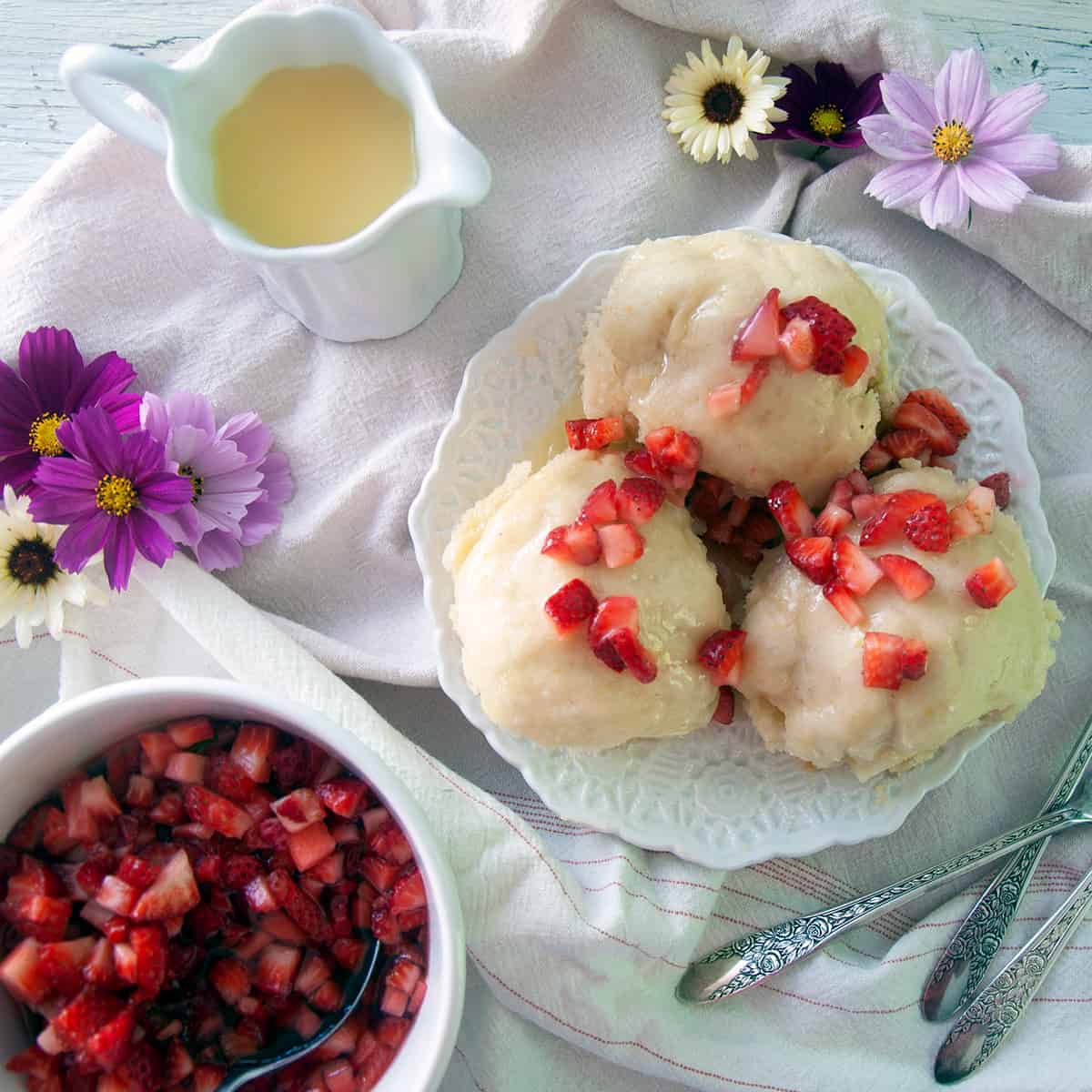 Three dampfnudel with strawberries on top.