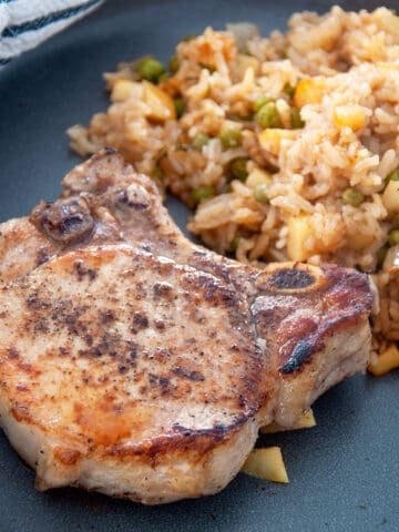 A single crispy pork chop with a serving of the apple rice medley behind it.