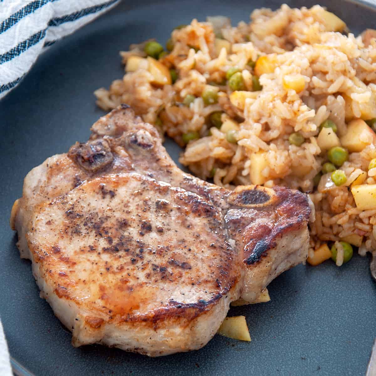 A single crispy pork chop with a serving of the apple rice medley behind it.