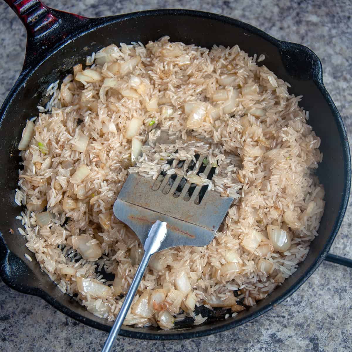 Rice and glassy onions with garlic in a cast iron pan.