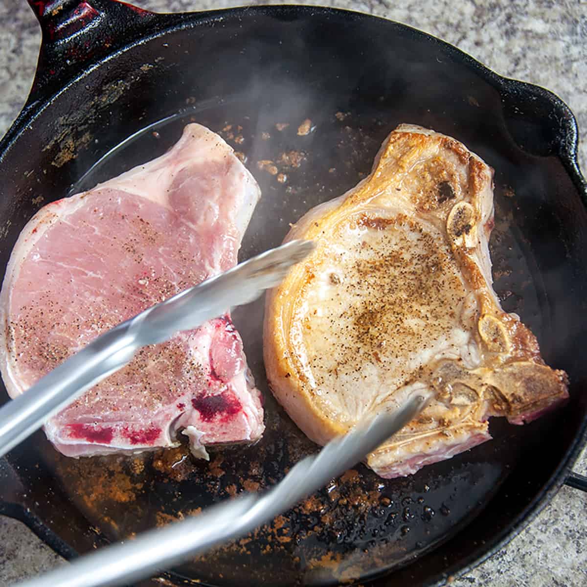 Two pork chops in a pan being seared.